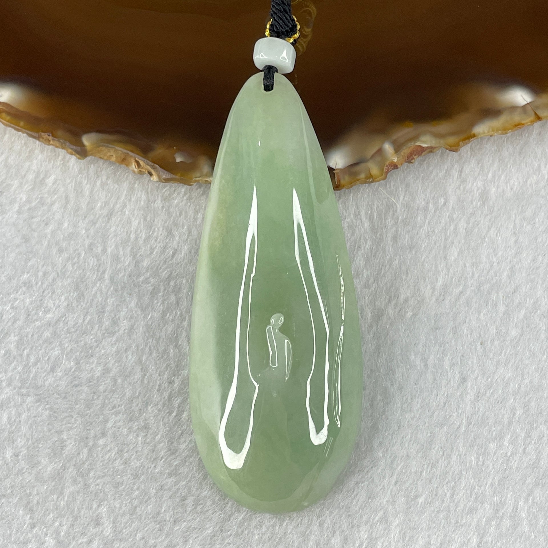Light green jadeite pendant with carved figure symbolizing enlightenment