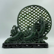 Dark green nephrite jade carving of three prawns in a net on wooden display stand