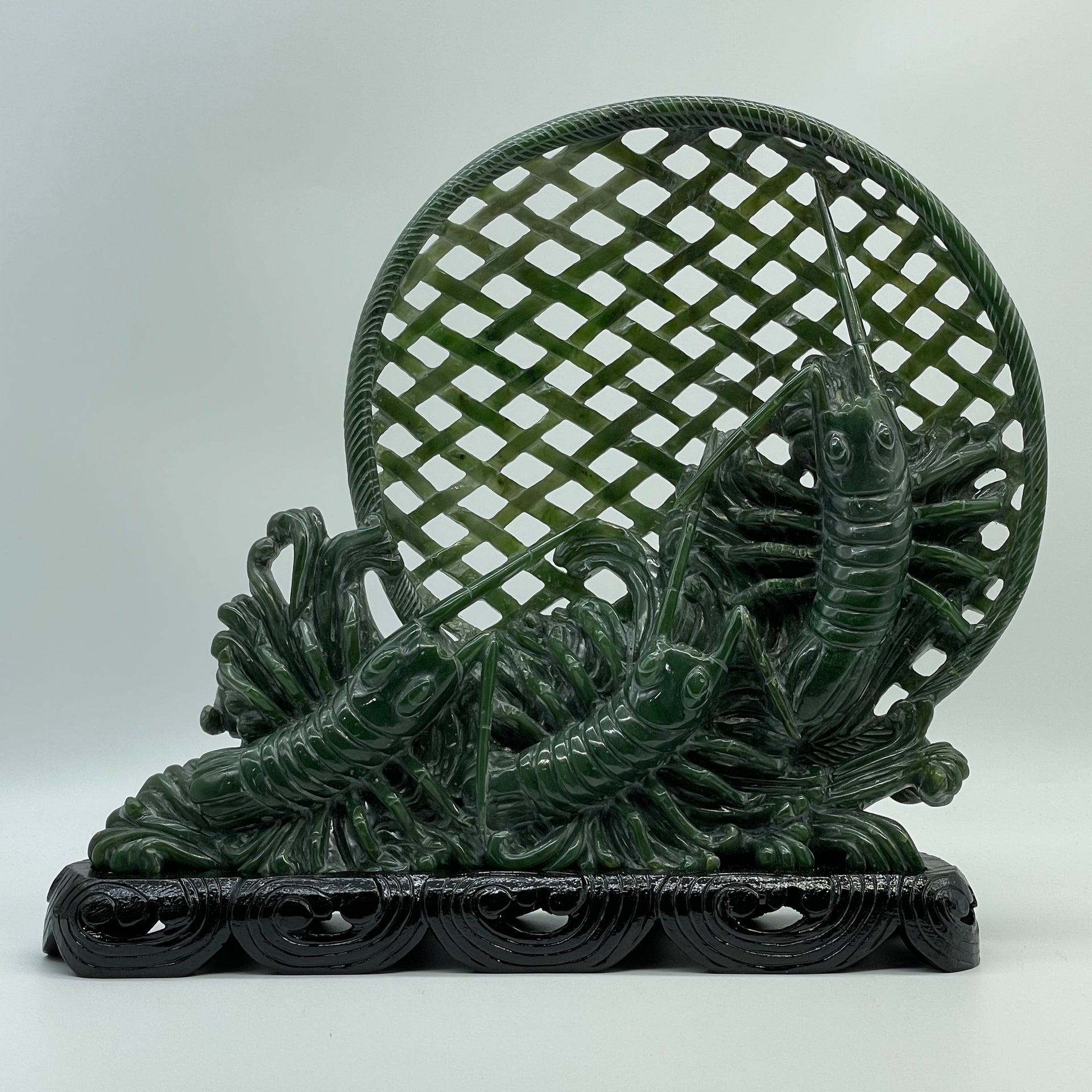 Dark green nephrite jade carving of three prawns in a net on wooden display stand