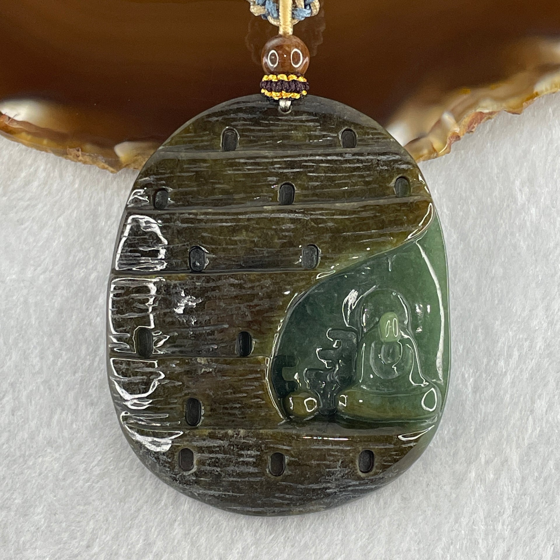 Brown and blue-green jadeite pendant with carved enlightenment motif on plain background